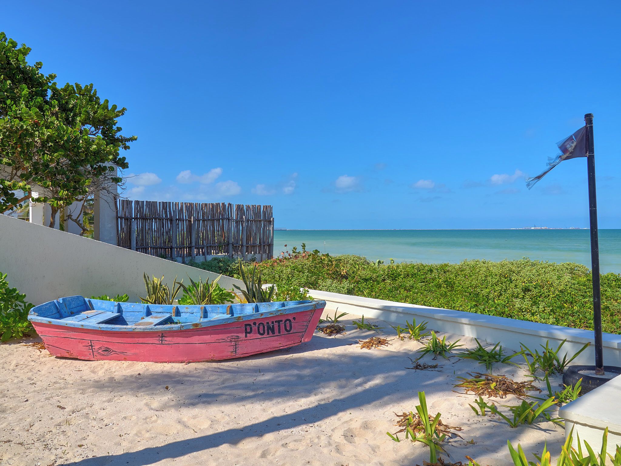 A red boat named 'P'ONTO' on a sandy beach with a clear blue sky and ocean in the background.