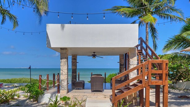 Une terrasse au bord de la plage, dotée d’un espace salon couvert, d’un escalier en bois et offrant une vue sur l’océan.