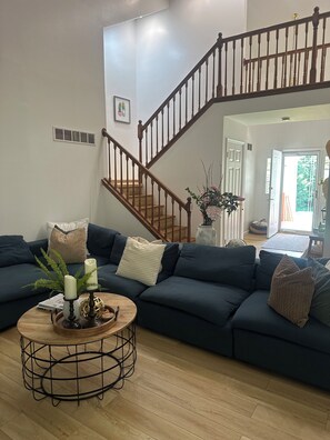 A living room with a dark green sectional sofa, a round coffee table with candles, a staircase, and a door leading outside. - Experience Nature In Comfort (Tobyhanna)