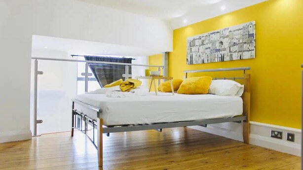 Une chambre à coucher moderne avec un lit, une fenêtre avec des rideaux, un tableau au mur et un plancher en bois.