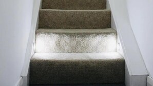 Un escalier recouvert de moquette, avec des murs blancs et un mur d’accent jaune.