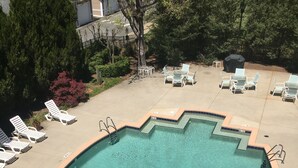 Une piscine dont le bord est revêtu de carrelage, entourée de chaises longues et dotée d’un espace barbecue couvert.