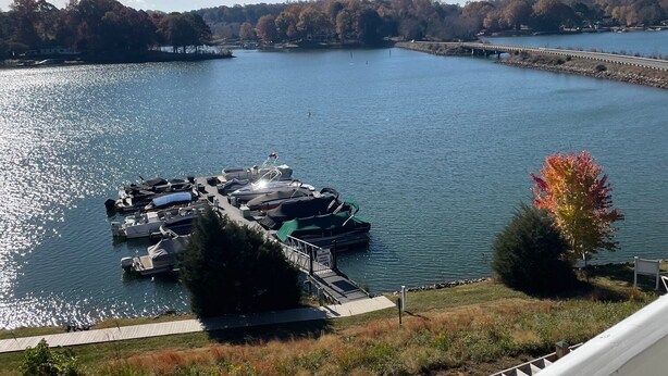 Un quai au bord de l’eau avec des bateaux, un ciel dégagé et une zone boisée en arrière-plan.
