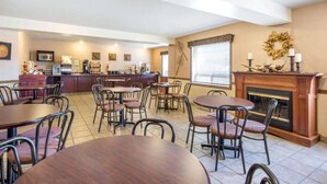Un'area pranzo con tavoli e sedie rotonde, una cucina sullo sfondo e un caminetto decorato con un'corona.