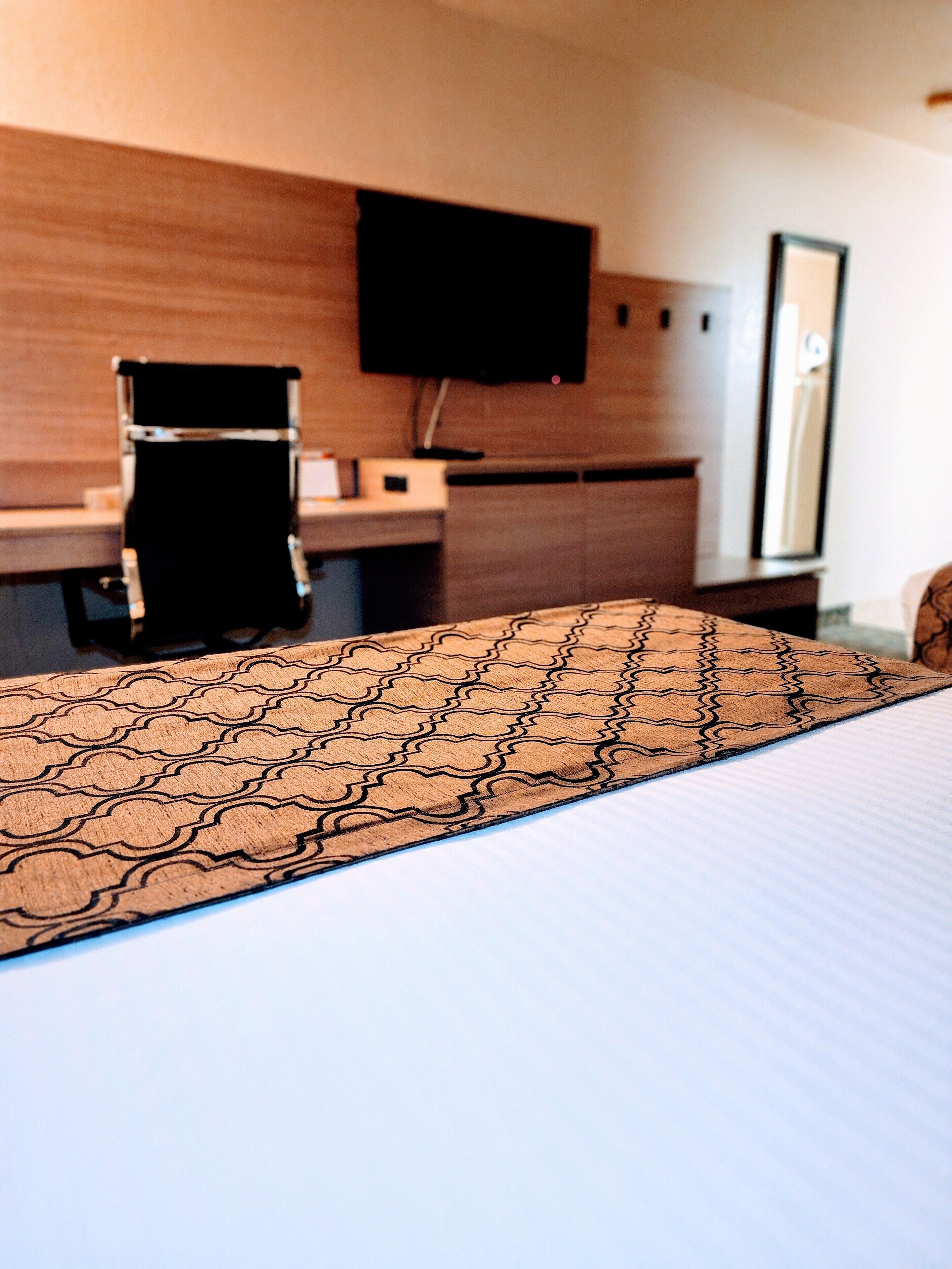 A hotel room with a bed, a desk, a chair, a flat-screen TV, and a mirror.