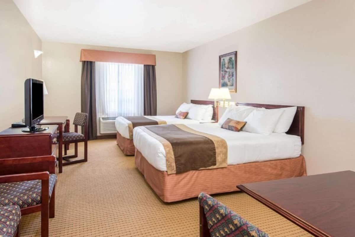 A hotel room with two beds, a desk, a chair, a TV, and a window with curtains.