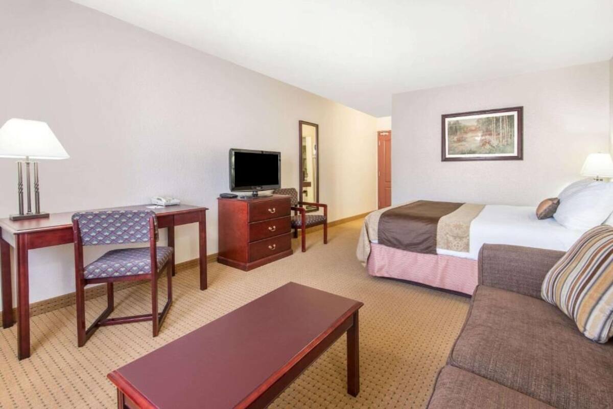 A hotel room with a bed, a desk with a chair, a dresser, a television, and a painting on the wall.