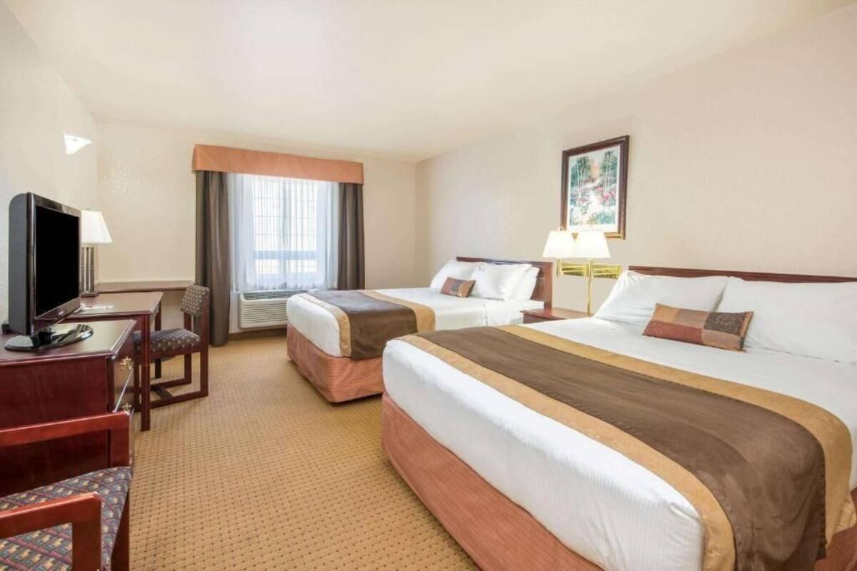 A hotel room with two beds, a desk with a chair, a television, and a window with curtains.