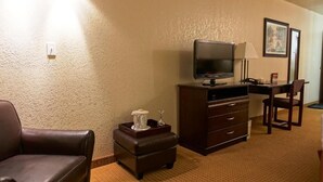 Una camera d'albergo con una poltrona in pelle, un tavolino con vassoio, una televisione su un mobile, una scrivania con lampada e un quadro appeso al muro.