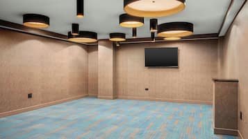 A conference room with a blue carpet, a flat-screen TV mounted on the wall, and multiple ceiling lights.