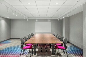 Une salle de conférence avec une longue table, des chaises, un écran de projection et une moquette à motifs.