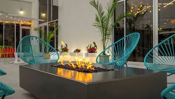 A modern outdoor seating area with a central fire feature, surrounded by teal chairs and potted plants.