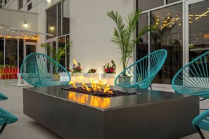 A modern outdoor seating area with a central fire feature, surrounded by teal chairs and potted plants. - Aloft by Marriott Chicago Schaumburg (Rolling Meadows)