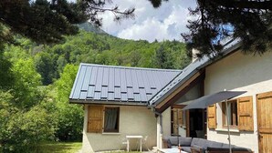 A rustic chalet with a sloped roof, wooden shutters, and a small patio area with outdoor seating. - SUPERB HOUSE, GREAT LOCATION - SLEEPS 10 (Allemont)