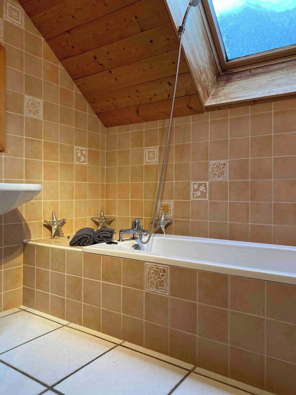 Un baño con techo de madera, una bañera, una ducha y azulejos decorativos.
