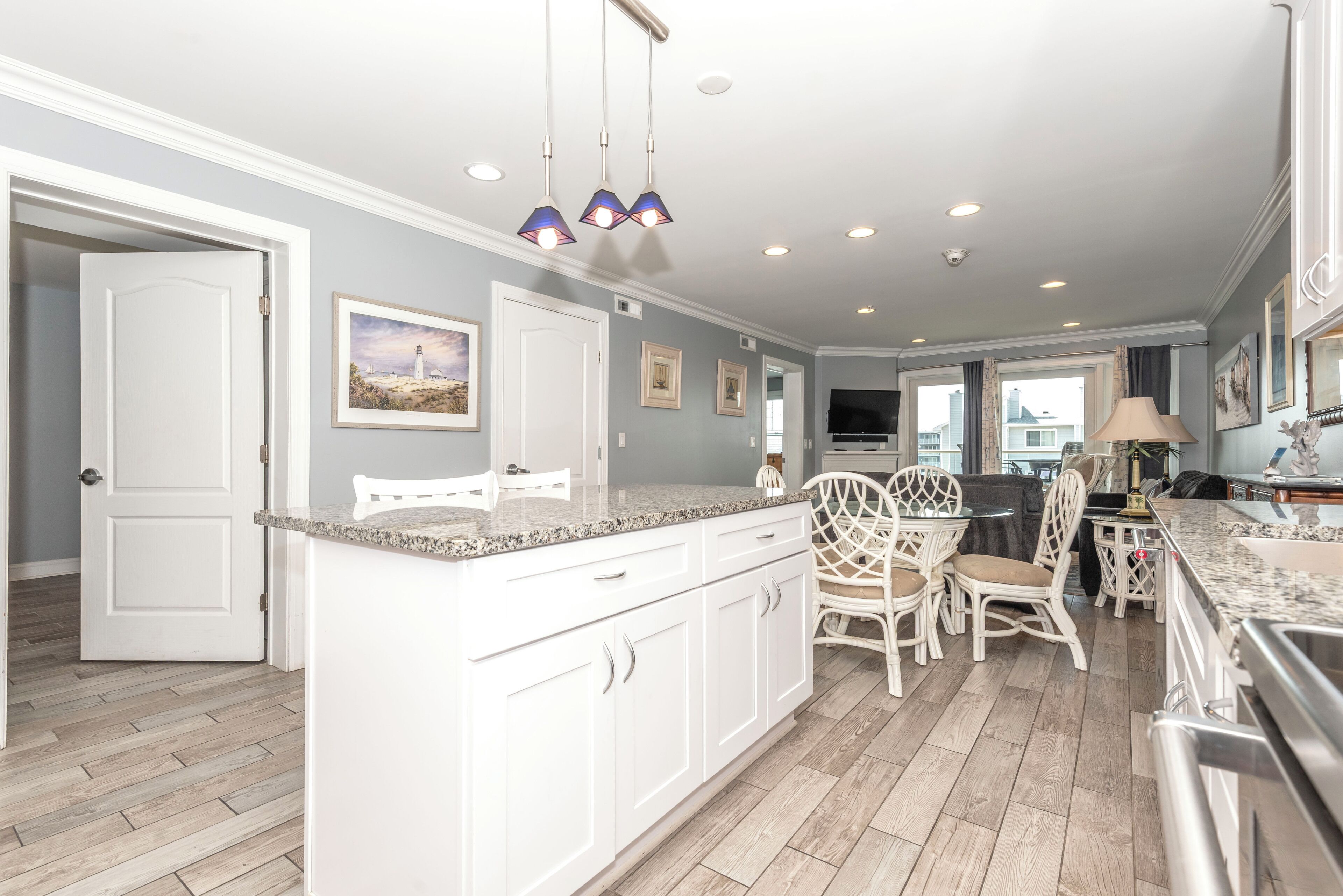 A kitchen with white cabinets, a granite countertop, wicker chairs, and pendant lighting.
