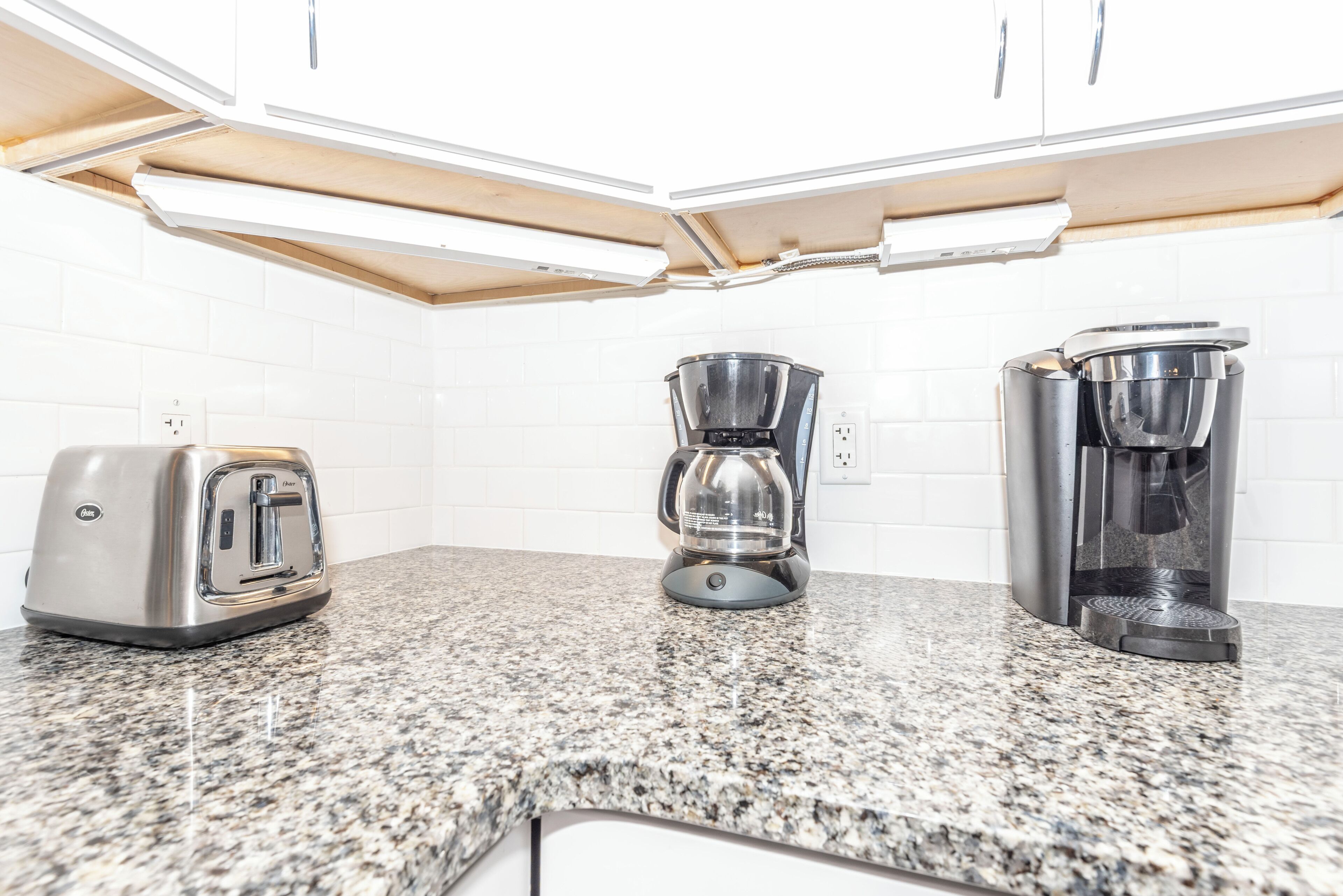 A kitchen with a toaster, a coffee maker, and a kettle on a granite countertop.