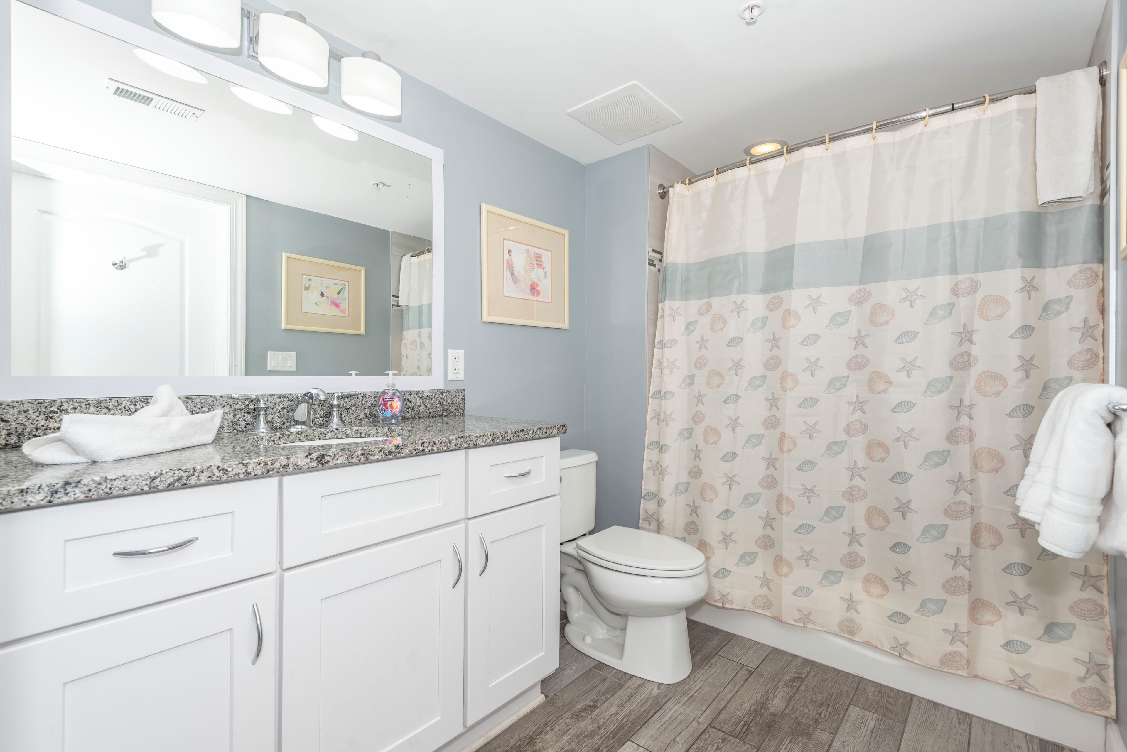 A bathroom with a white toilet, a sink with a granite countertop, and a shower curtain with a sea shell pattern.