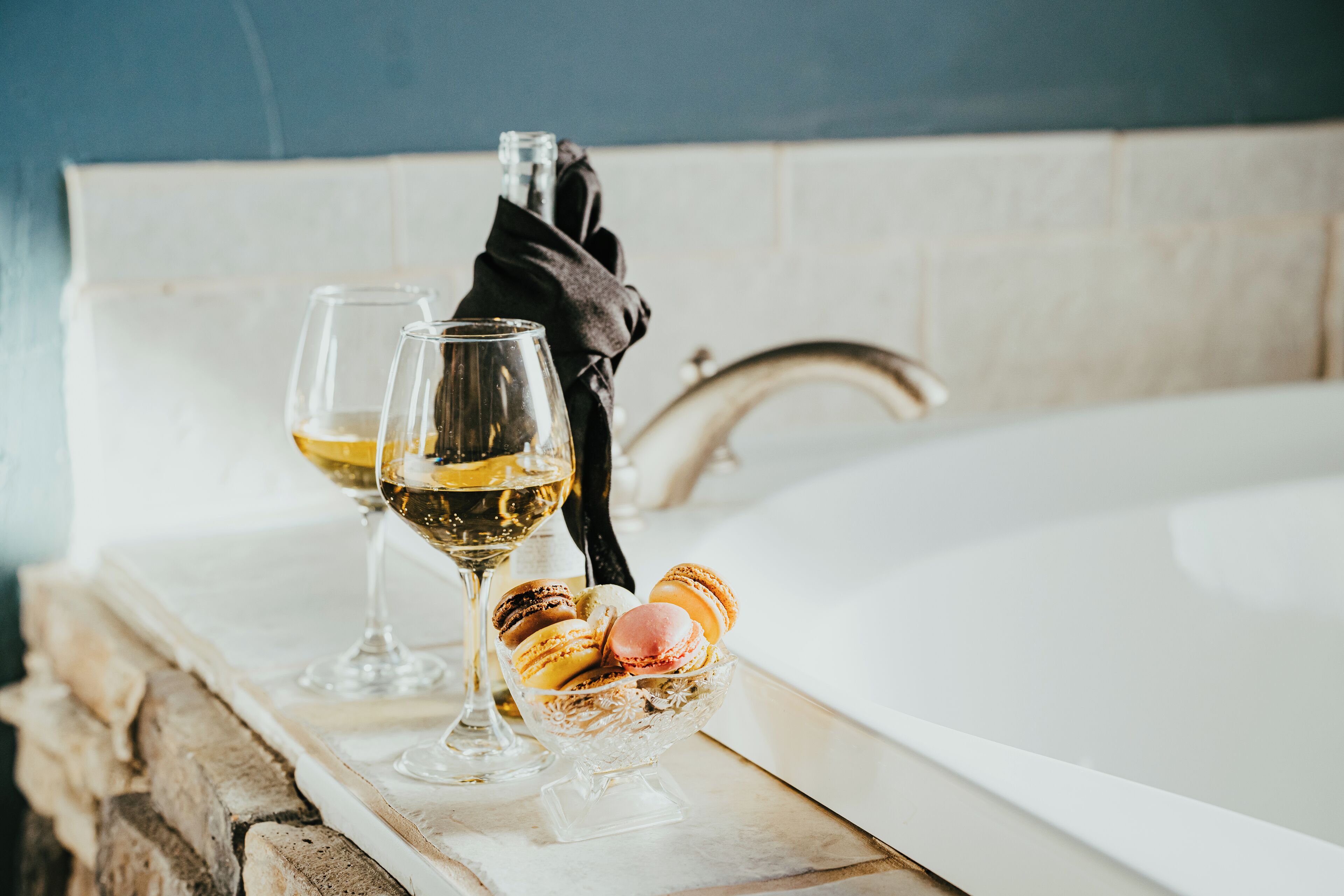 A bathtub with two glasses of wine and macarons on a marble surface.