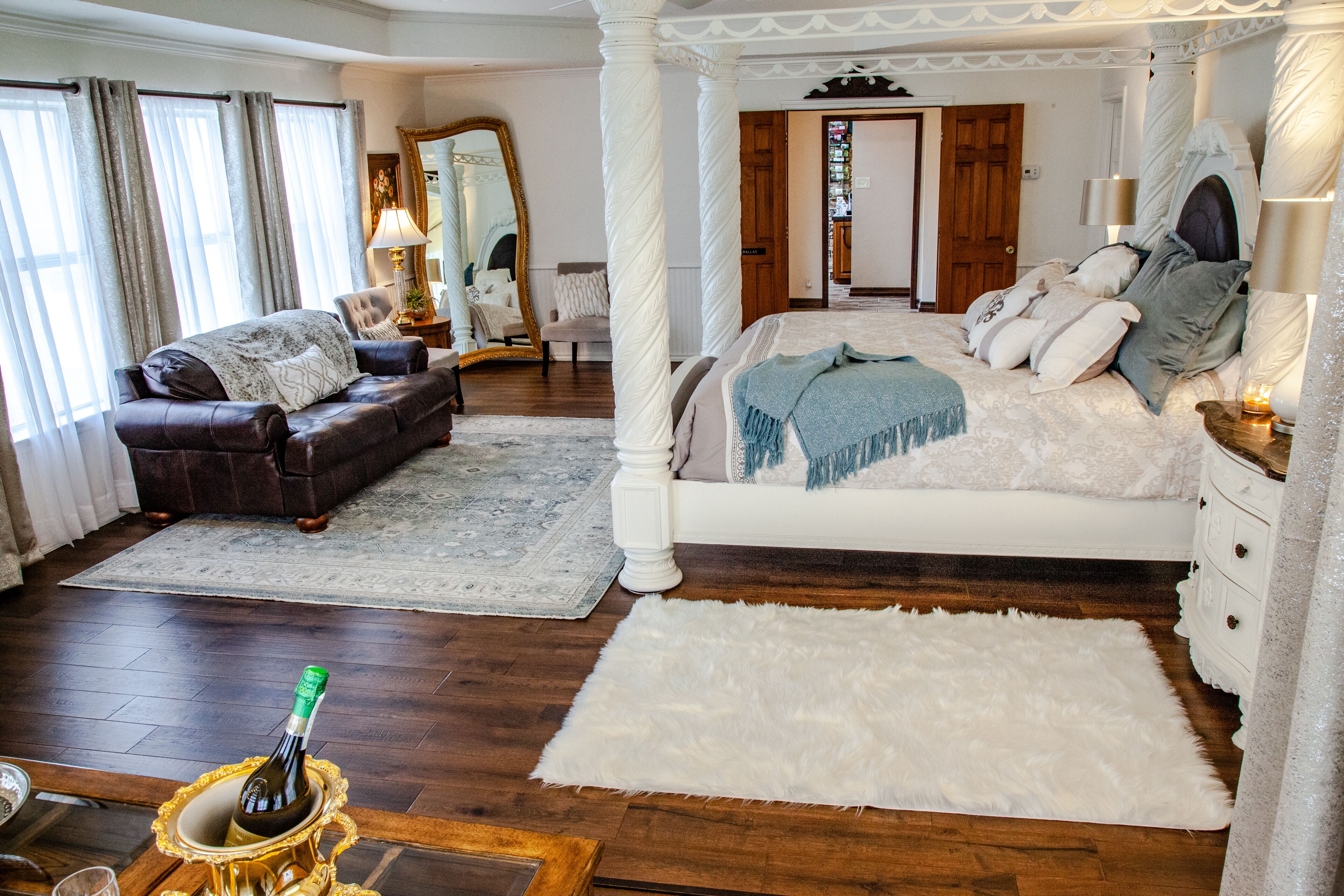 A bedroom with a four-poster bed, a sitting area with a sofa, and a large mirror.