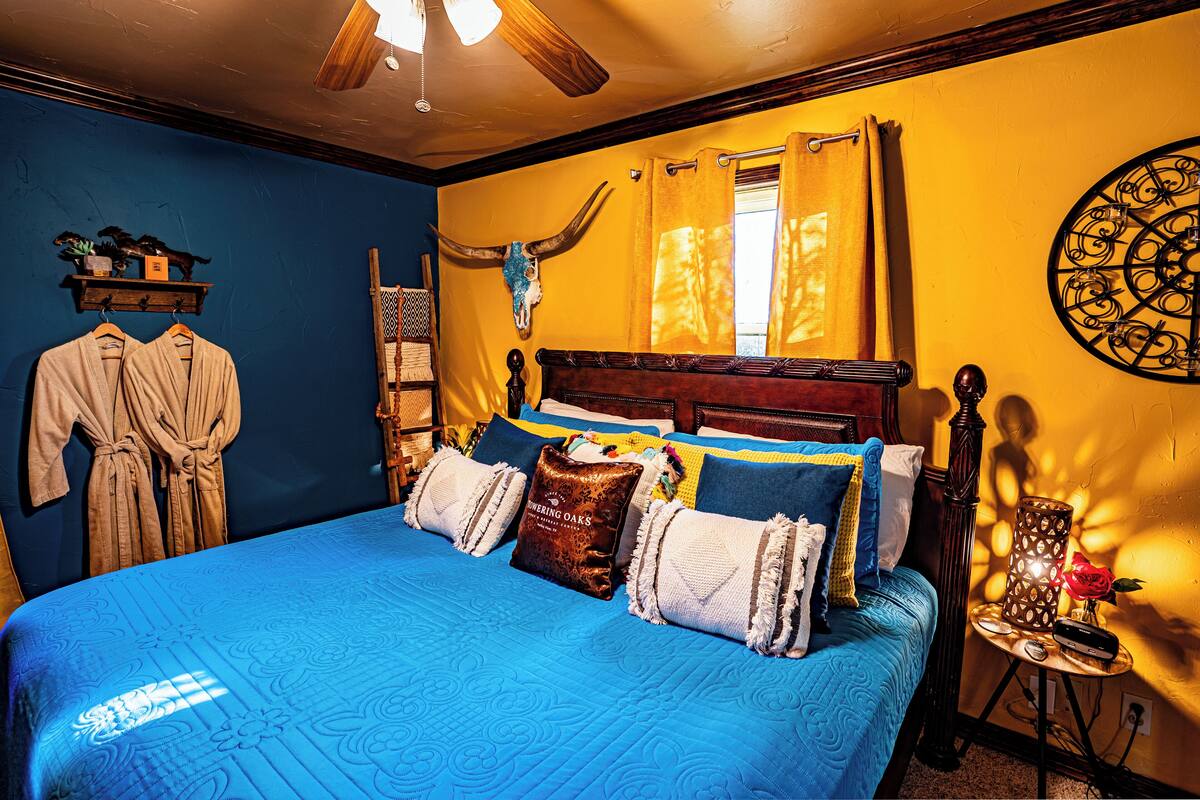 Ein Schlafzimmer mit einem großen Bett, einem Holzkopfteil, einem Deckenventilator, einem Nachttisch mit Lampe und einer Wanddekoration.