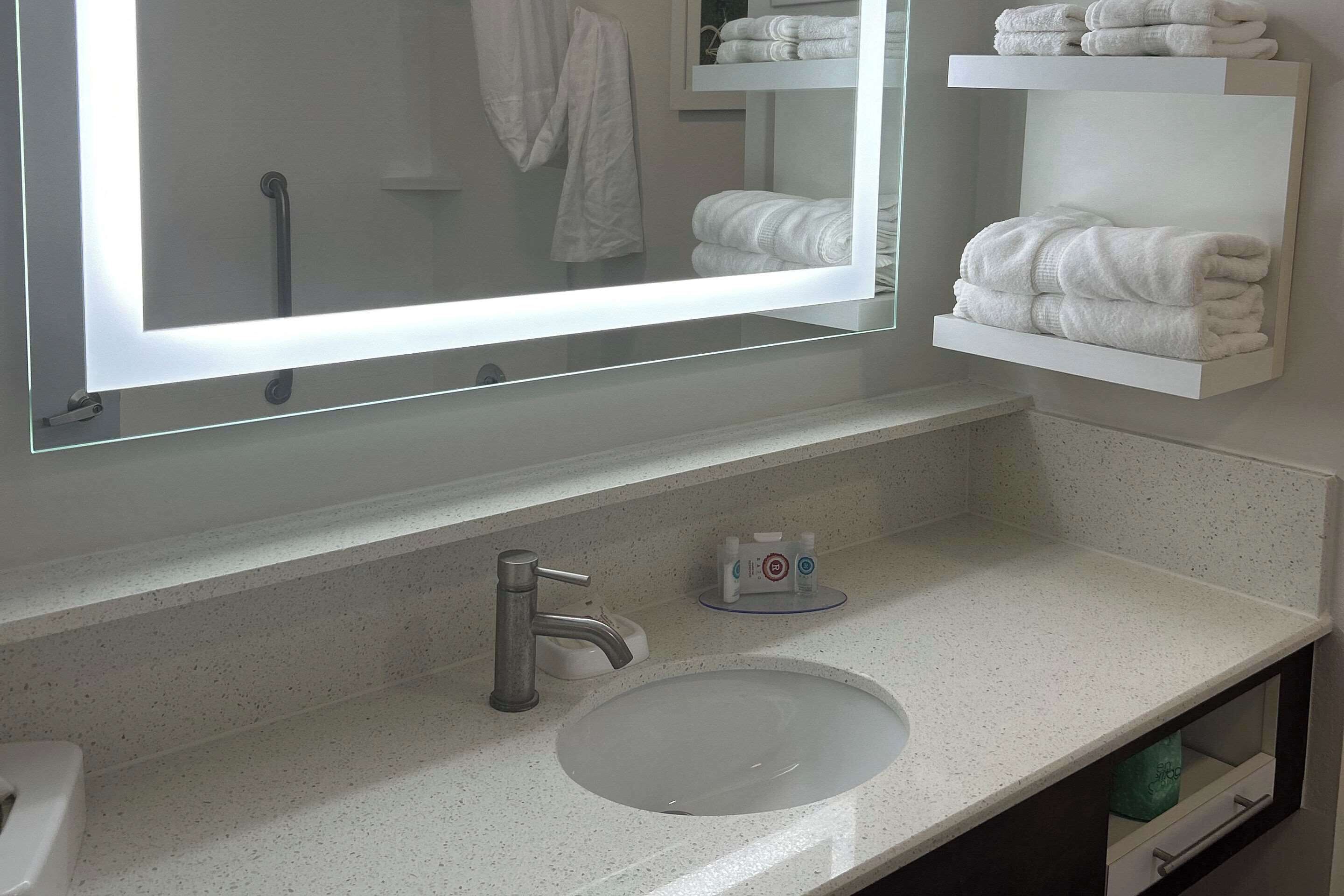 A bathroom with a large mirror, a sink, and towel storage.