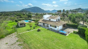 A white villa with a tiled roof, a swimming pool, and a tennis court.