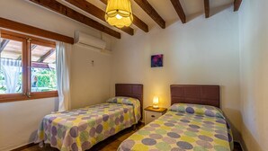 A bedroom with two beds, a window, a ceiling fan, and a painting on the wall.