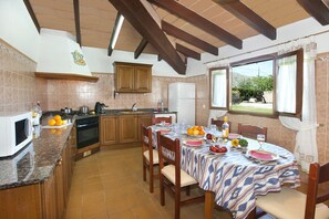 A kitchen with wooden cabinets, a stove, and a dining table set for four with a patterned tablecloth.