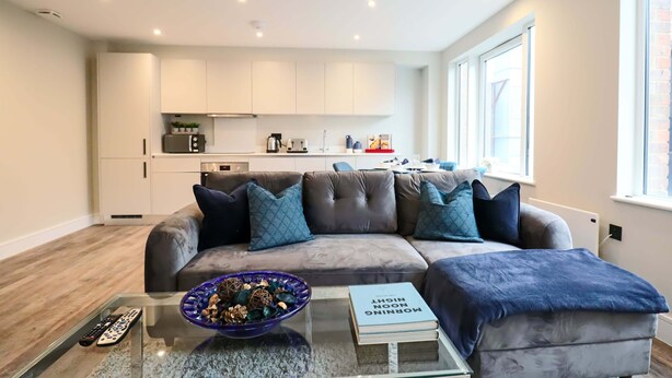 Ein modernes Wohnzimmer mit grauem Sofa, einem Glastisch und einer Fernbedienung.