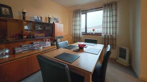 A dining area with a wooden table, chairs, a television, and a window with curtains.