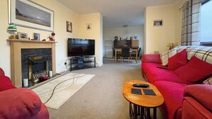 A living room with a fireplace, a TV, a dining area, and a red sofa.
