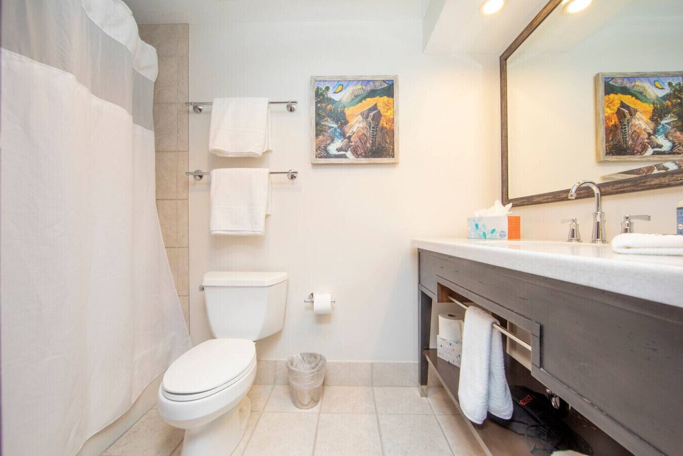A bathroom with a toilet, sink, and shower area. There are towels hanging on the wall and a trash bin on the floor.