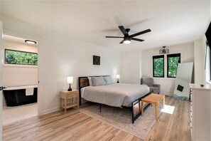A bedroom with a bed, bedside tables, a ceiling fan, a window, and a view of greenery outside. - 2BR + 2BA Lake Chatuge Cabin w/ Mountain Views! (Hiawassee)