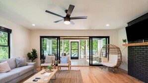Ein modernes Wohnzimmer mit Sofa, Couchtisch und Sesseln, Deckenventilator und Kamin.