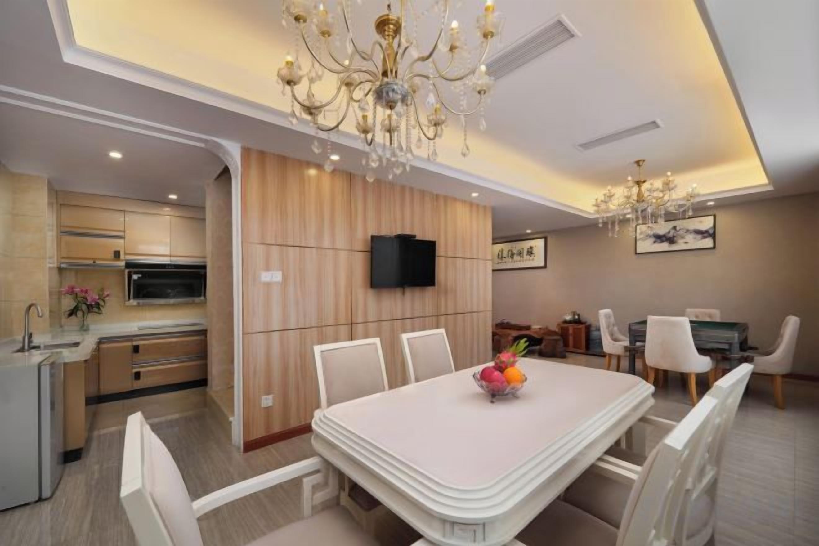 Una cocina moderna con electrodomésticos integrados, un comedor con mesa y sillas blancas, y una araña.