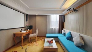 Une chambre d’hôtel avec un canapé, un bureau, une table basse avec des fruits, une télévision et une fenêtre avec des rideaux.