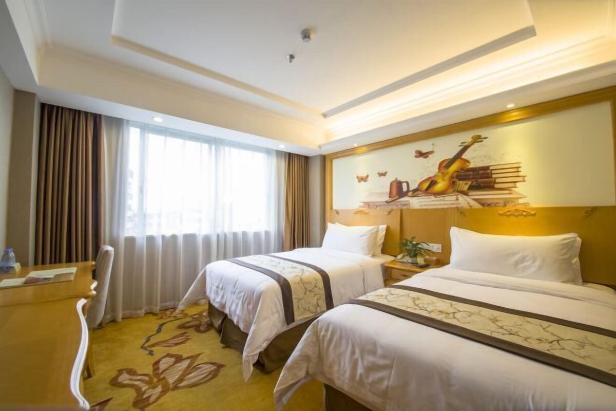 A hotel room with two beds, a desk, and a large window.