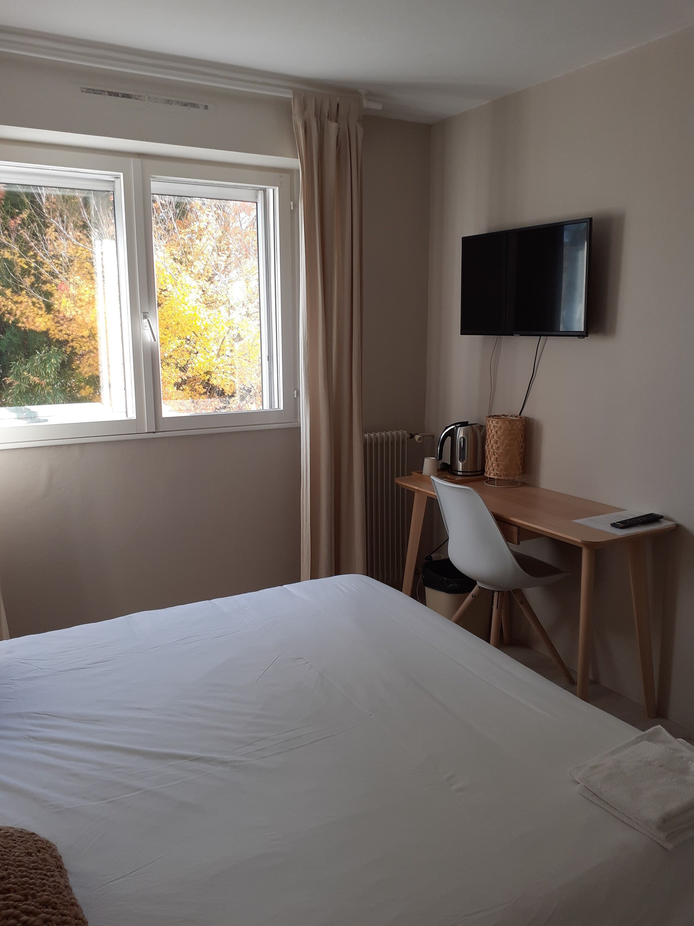 A hotel room with a bed, a desk with a chair, a television, and a window with curtains.