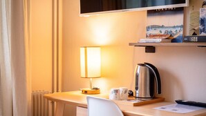 Ein Hotelzimmer mit Schreibtisch, Stuhl, Fernseher, Lampe, Wasserkocher und Heizkörper.