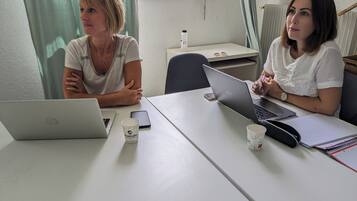 Dos personas sentadas a una mesa con computadoras portátiles, un teléfono inteligente y un cuaderno.