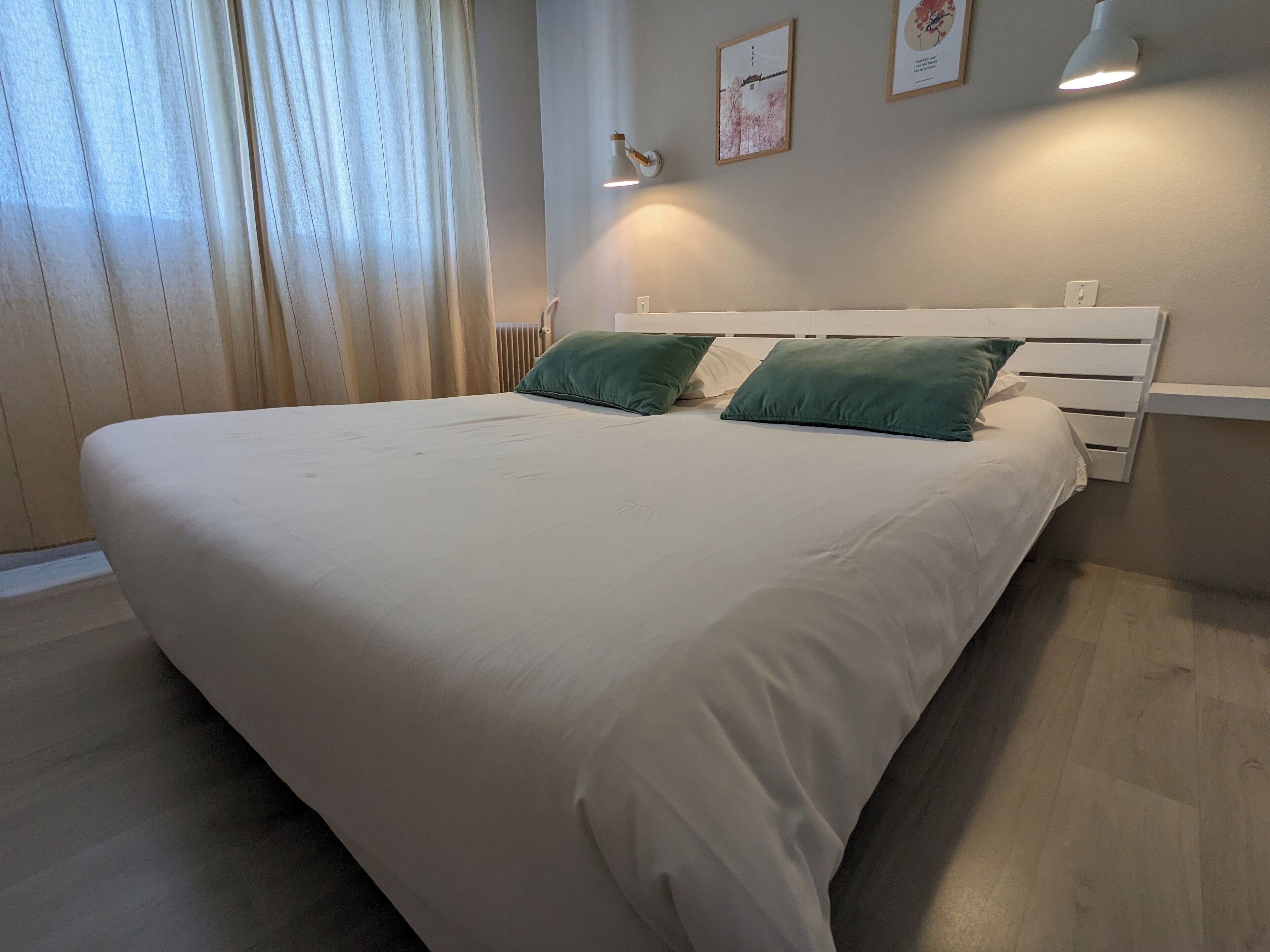 A neatly made bed with white bedding and two green pillows, a white headboard, and a bedside lamp.