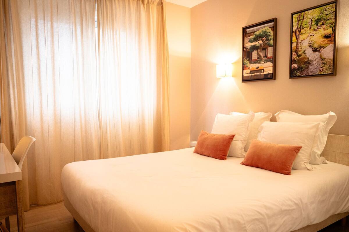 A hotel room with a bed, a desk, and two wall-mounted pictures.