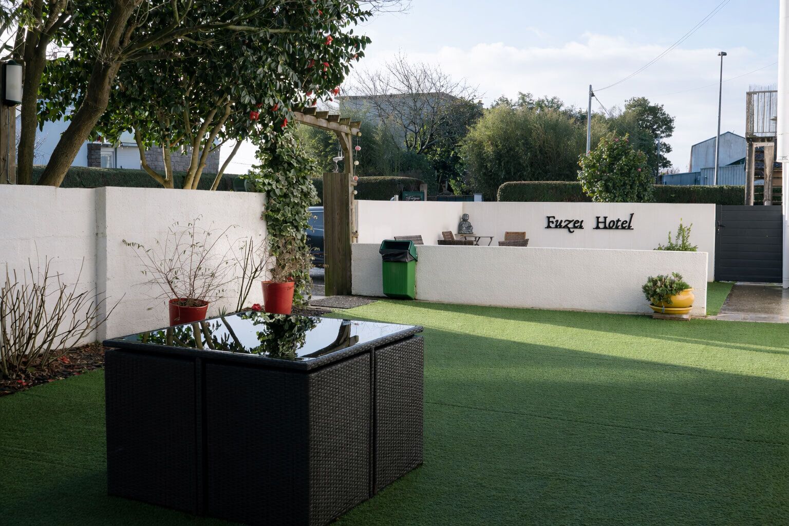 A hotel entrance with a white wall, a sign reading 'Fuzei Hotel,' and a green lawn.