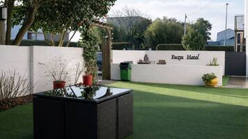 A hotel entrance with a white wall, a sign reading 'Fuzei Hotel,' and a green lawn.