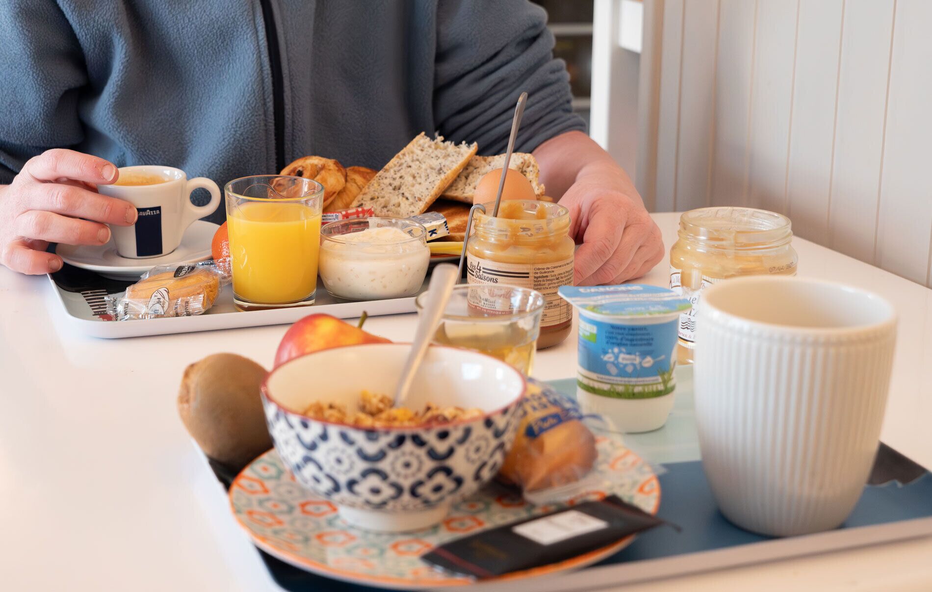 A breakfast tray with a cup, orange juice, bread, a bowl of cereal, a jar of jam, a mug, and a small container of butter.