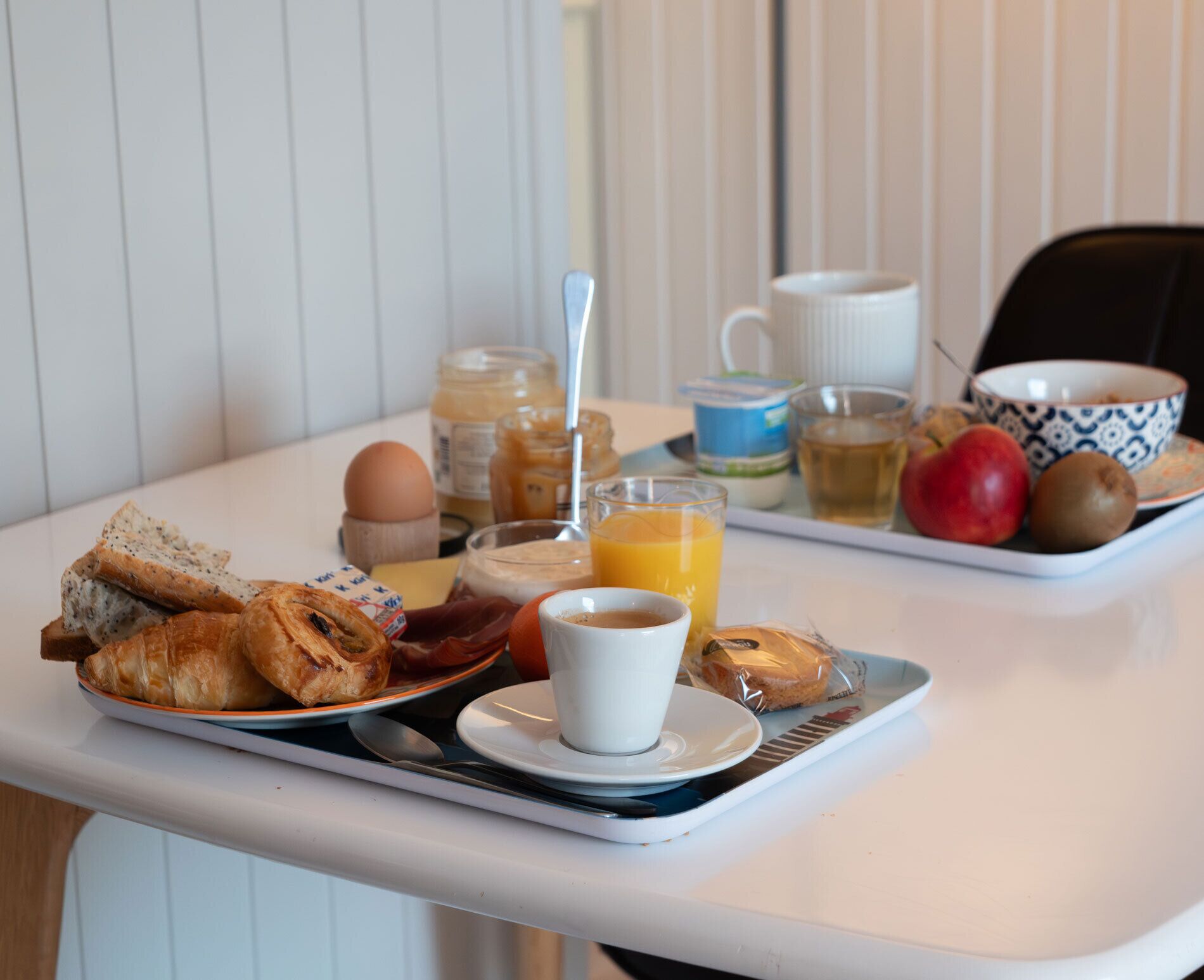Bandeja de desayuno con cruasanes, una taza de café, un vaso de jugo de naranja, un tazón de fruta y un frasco de miel.