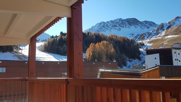 A wooden deck with a view of snow-covered mountains and a forest.