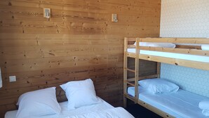 A bunk bed with white bedding in a room with wooden walls and hexagonal patterned wallpaper.