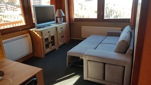 A compact room with a bed, a TV, a desk, and a window with curtains.